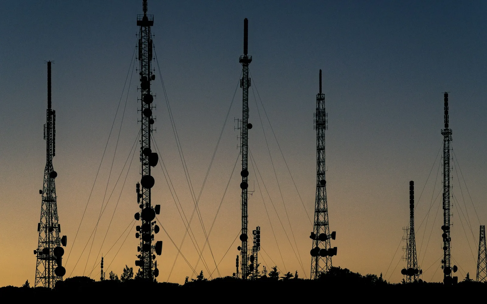 Telecommunication towers and antennas silhouetted at sunset.